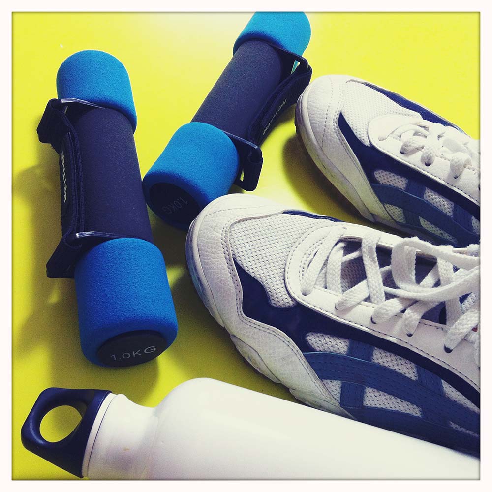 Ein paar Laufschuhe und Hanteln auf einem gelben Untergrund.